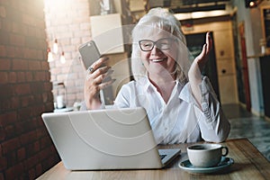 Happy businesswoman sitting at table in front of laptop, holding