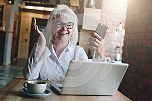 Happy businesswoman sitting at table in front of laptop, holding