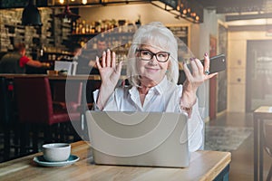 Happy businesswoman sitting at table in front of laptop, holding hands up and smiling, working, learning.