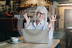 Happy businesswoman sitting at table in front of laptop, holding hands up and smiling, working, learning.