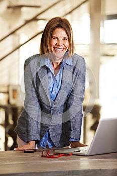 Happy businesswoman standing by desk with laptop computer