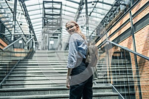 Happy businesswoman or student with backpack climbing the stairs in modern loft style hall. Road to success concept