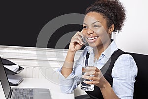 Happy businesswoman using cell phone in front of laptop at desk in office