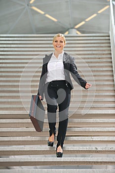 Happy businesswoman walking downstairs with briefcase