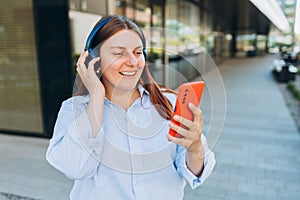 A happy businesswoman walking outdoors and having phone calls over earbuds. Busy woman with a phone and earphones near