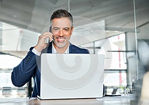 Happy busy middle aged business man talking on phone using laptop in office.