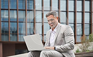 Happy busy middle aged business man working on laptop outside office.