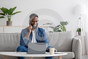 Happy busy millennial african american businessman freelancer with beard looks at pc, call to client by phone
