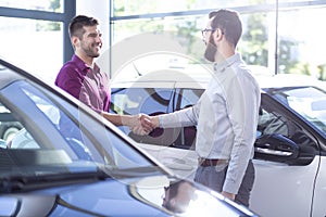 Happy buyer of new car shaking hands with dealer after transaction in the salon