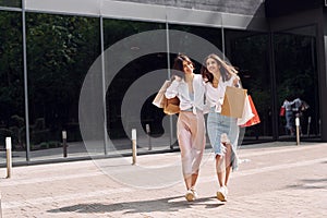 Happy buyers. Two female friends have a shopping day. Walking outdoors with bags