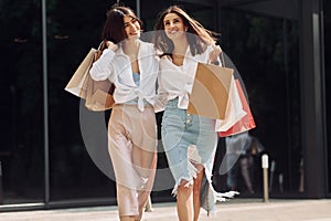 Happy buyers. Two female friends have a shopping day. Walking outdoors with bags