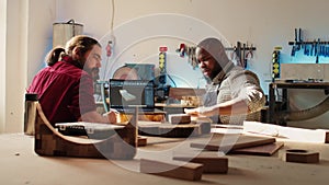 Happy cabinetmaker and colleague comparing wood piece with schematic