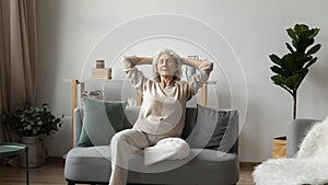 Peaceful elderly woman relax on couch meditating