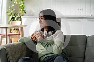 Smiling relaxed female sitting on sofa at home holding cup of tea and relaxing after stressful day