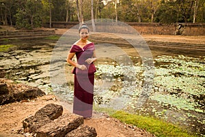 Happy Cambodian Asian Girl in Traditional Dress Stands by a Pool of Water in Angkor Thom near Temple
