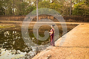 Happy Cambodian Asian Girl in Traditional Dress Stands by a Pool of Water in Angkor Thom near Temple