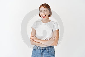 Happy candid woman in t-shirt and jeans, winking and smiling at camera, motivating you, cross arms on chest and look