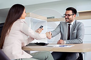 Happy car dealer and customer shake hands after successfully signed contract.