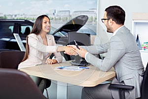 Happy car dealer and customer shake hands after successfully signed contract.