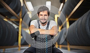 Happy car mechanic with tire in tire store