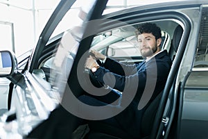 Happy car owner at the dealership. Handsome young men sitting at front seat of the car looking at camera