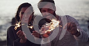 Happy, carefree and celebrating couple playing with sparklers outdoors on the beach on a windy day. Excited, cheerful