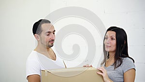 Happy carefree couple having fun together, flirting, then hiding behind big cardboard box in their new house.