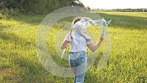 Happy carefree kid runs across the field with soap bubbles. Childhood dream concept. Little girl has fun playing