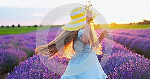 Happy carefree little girl with beautiful dress running in lavender field rows at sunset