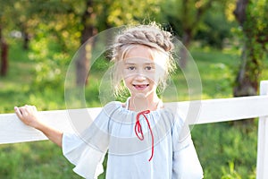 Happy carefree little girl smiling leaned on wooden rustic fence on  background of farm and garden. Copy space. Kid at ranch. rela