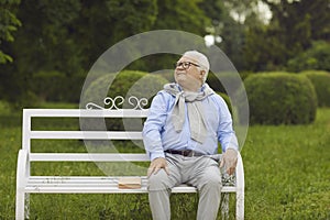 Happy carefree senior man sitting on wooden bench relaxing on sunny day in park