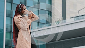 Happy carefree stylish young african american woman listening to music on smartphone with headphones outdoors joyful