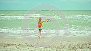 Happy carefree woman in hat running from camera to sea water, enjoying on the beach, sea waves and cloudy sky background