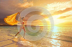 Happy carefree woman running in the sunset on the beach.