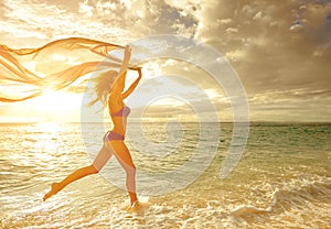 Happy carefree woman running in the sunset on the beach.