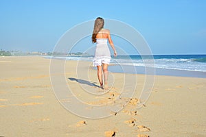 Happy carefree woman walking on beach celebrating her freedom. Summer woman background of the ocean and sand. Back view of girl.