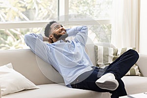 Happy carefree young African man relaxing on cozy home couch