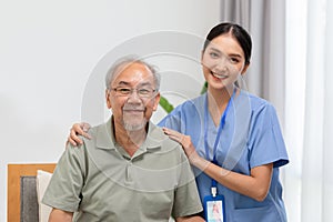 Happy caregiver and elderly patient smile and looking camera nursing at home. Asian senior man and doctor giving care and empathy