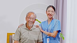 Happy caregiver and elderly patient smile and looking camera nursing at home. Asian senior man and doctor giving care and empathy