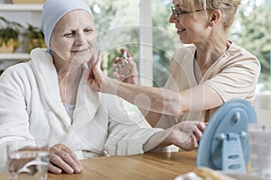 Happy caregiver spraying perfumes on sick senior woman with breast cancer photo
