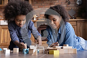 Happy caring African American mother with little daughter building tower