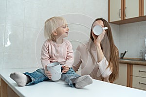 Happy caring mum and fair-haired girl drink milk at the kitchen