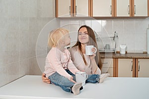 Happy caring mum and little blond girl take a breakfast at the kitchen