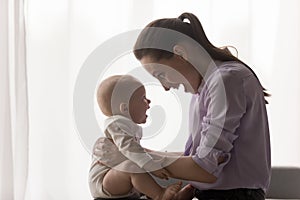 Happy caring young mother holding on laps baby.