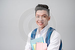 Happy casual asian male student holding books isolated on a gray