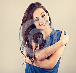 Happy casual happy woman hugging herself with natural emotional face on blue background. Closeup toned vintage