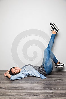 Happy casual woman lying on the floor with raised legs up over gray background and looking at camera