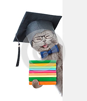 Happy Cat with black graduation cap holding books and peeking from behind empty board. isolated on white background