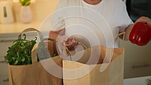 Happy Caucasian 60s woman sort vegetables from eco package in minimalist kitchen. Online buying food and grocery