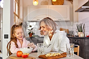 Happy caucasian adult woman and child girl have breakfast in the kitchen at home